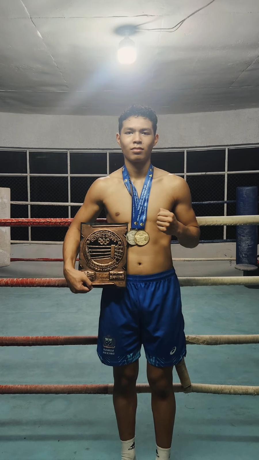 SUBA boxer in Samoa kit holding two medals and the Team Samoa plaque in the ring