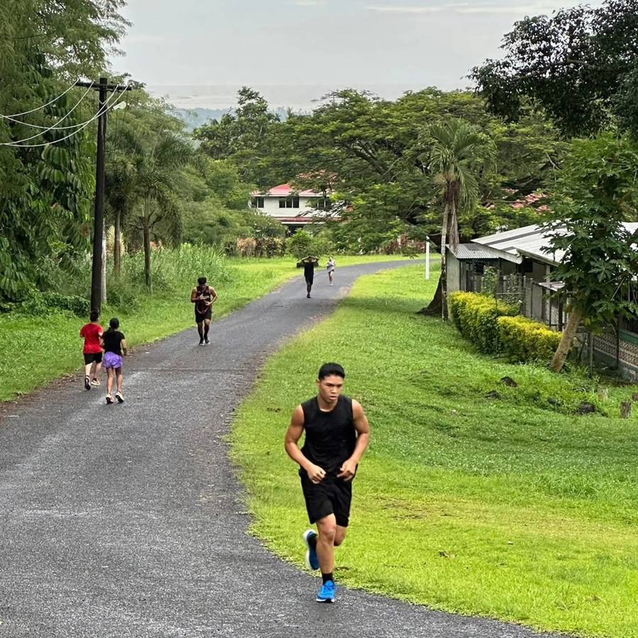 Boxers and kids on an uphill road run through green Samoan countryside