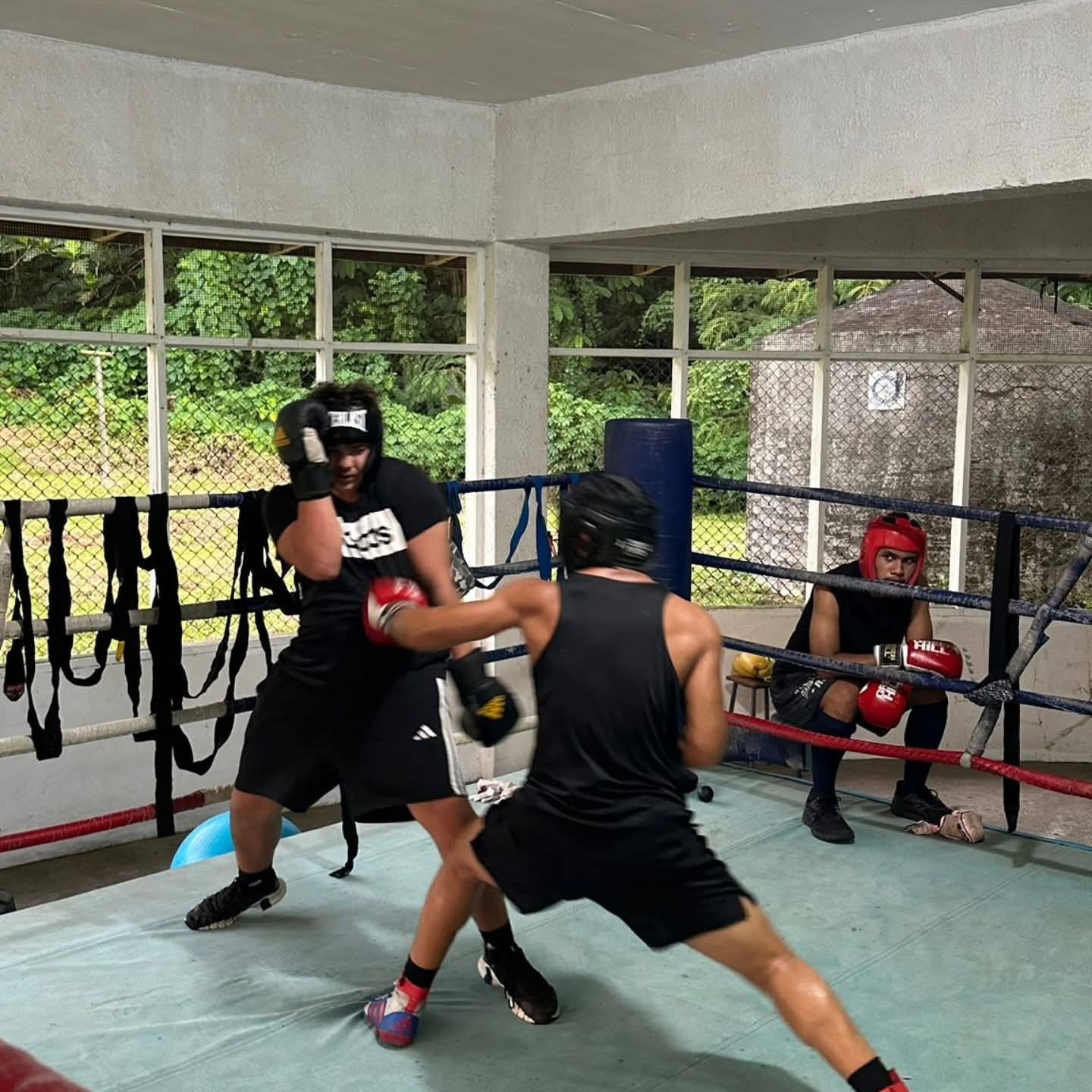 Two boxers sparring while a teammate waits ringside